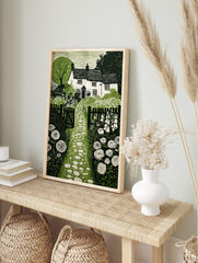 Cottage garden green linocut print with house, stone path, picket fence, foxgloves, and, in an alternate framed mockup