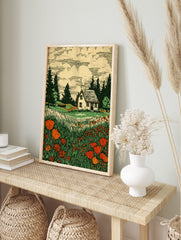 Woodcut print of a white cottage in a field of red poppies and tall green grass with pine, in an alternate framed mockup