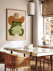 Green frog wearing a brown cowboy hat in a painterly illustrative style art print, in a styled room mockup
