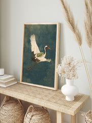 Illustrative art print of a white crane flying with a green frog on its back, over a deep, in an alternate framed mockup