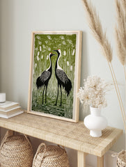 Linocut style print of two black and white crane birds with red crowns in a green marsh with, in an alternate framed mockup