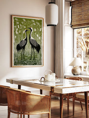 Linocut style print of two black and white crane birds with red crowns in a green marsh with, in a styled room mockup