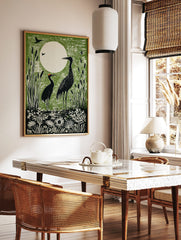 Green linocut print of two black cranes in a marsh with cattails and a large white moon in the, in a styled room mockup