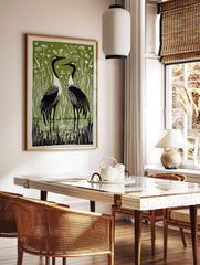 Two black and white cranes in reeds and water, with white hearts on a green background, in a, in a styled room mockup