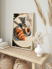 Watercolor-style illustration of a croissant on a striped plate with coffee and a knife, in an alternate framed mockup