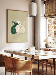 Illustrative print of two cuddling rabbits, one dark green with stars, one beige with a grid, on a, in a styled room mockup