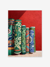 Cultural wall art print depicting several vibrantly patterned, rolled green, blue, and orange textiles against a red wall.