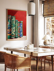 Cultural wall art print depicting several vibrantly patterned, rolled green, blue, and orange textiles against a red wall. - Image 2