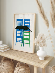 Black dachshund dog silhouette resting on stacked blue and green chairs, graphic illustration, in an alternate framed mockup