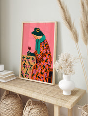 Whimsical painting of a frog in an orange floral robe, teal scarf, holding a wine glass, in an alternate framed mockup
