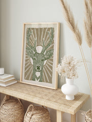 Stylised green deer head with antlers and sunburst on beige background, linocut style animal, in an alternate framed mockup