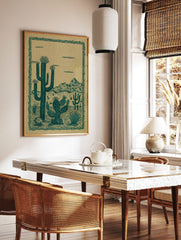 Illustrative desert landscape print with teal green saguaro and prickly pear cacti against a tan, in a styled room mockup