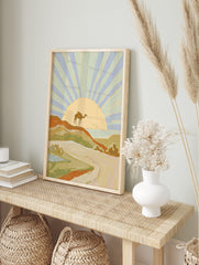 Illustrative desert landscape art print with a camel on a dune, radiating sunset, and distant, in an alternate framed mockup