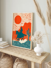 Illustrative Western art print of cowboy on horse against orange sun and desert landscape, in an alternate framed mockup