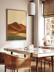 Illustrative desert landscape print with brown mountains, sandy foreground, and yellow flowers, in a styled room mockup