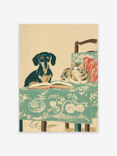 Illustrated dog and cat wall art with a dachshund and tabby cat reading a book on a green patterned tablecloth.