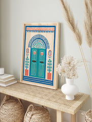 Illustrative doorway wall art print with an arched blue door, red accents, and potted plants on a cream background, folk art style. - Image 3