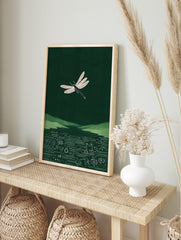 White dragonfly illustration flying over green hills and a circuit board pattern in dark, in an alternate framed mockup