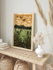 Linocut print of three black dragonflies flying over a green lake with cattails and mountains, in an alternate framed mockup