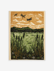 Lino cut style art print of three dragonflies flying over a lake with cattails and mountains under an orange sky