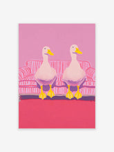 Two white ducks with yellow beaks and feet sitting on a pink and white striped couch in pink room. Duck wall art.