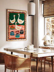 Folk art print of three white ducks, croissants, and coffee cups on green and pink striped, in a styled room mockup