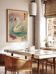 Elegant white swan with red beak swimming in water with ripples, Japanese text, and purple reeds, in a styled room mockup