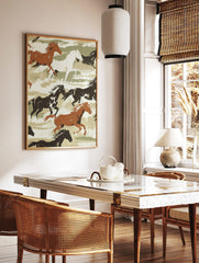 Illustrative print of galloping brown, black, and white horses on a green and beige brushstroke, in a styled room mockup
