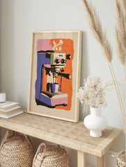 Illustrative print of a purple and orange espresso machine pouring coffee into a cup, with, in an alternate framed mockup