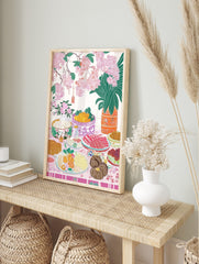 Illustrative art print of a festive table with food, pink cherry blossoms, and green foliage, in an alternate framed mockup