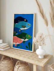 Illustrative print of five colourful fish in blue, green, and pink, swimming in deep blue, in an alternate framed mockup
