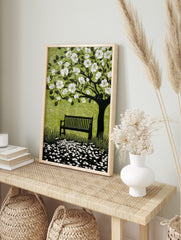 Linocut style print of a flowering tree with white blossoms, a dark bench, and scattered, in an alternate framed mockup