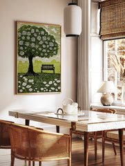 Linocut style print of a flowering tree, park bench, and wildflowers in a green field with white sky, in a styled room mockup