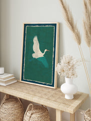 White crane with teal wings flying against a textured green background, framed by cream and, in an alternate framed mockup