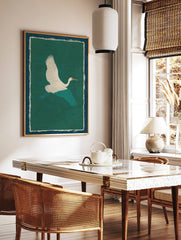 White crane with teal wings flying against a textured green background, framed by cream and blue, in a styled room mockup