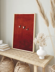 Three cranes with outstretched wings flying diagonally against a textured red background, in an alternate framed mockup