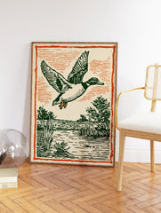 Vintage illustration of a flying duck with green feathers over a marsh and water, framed by an orange border. - Image 2