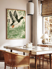 Linocut style print of a mallard duck in flight over water with reeds and foliage, in a styled room mockup