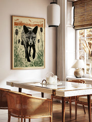 Linocut style print of a black fox walking through green reeds and brown grasses against a light, in a styled room mockup