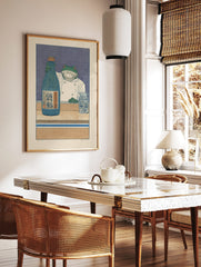Illustrative print of a frog chef holding a blue sake bottle with Japanese Kanji on a wooden counter, in a styled room mockup