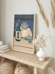 Ukiyo-e style print of a frog chef holding a green sake bottle with kanji, next to a, in an alternate framed mockup
