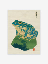 Vintage Japanese woodblock print of a blue-green and gold frog sitting on a dark green rock, with Japanese calligraphy.