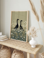 Two black geese with gold head markings standing in a field of white wildflowers on a beige, in an alternate framed mockup
