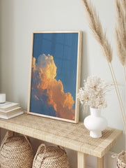 Close-up of cumulus clouds bathed in warm orange and yellow light against a blue sky, in an alternate framed mockup