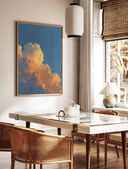Close-up of cumulus clouds bathed in warm orange and yellow light against a blue sky, in a styled room mockup