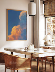 Dramatic golden orange sunset clouds against a clear blue sky, filling the frame with natural light, in a styled room mockup