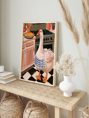 Illustration of a goose wearing a blue checkered apron standing in a kitchen next to a stove, in an alternate framed mockup