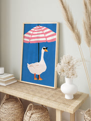 Playful illustration of a white goose in sunglasses under a pink and white striped beach, in an alternate framed mockup