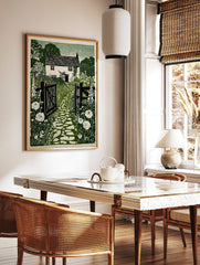 Green linocut print of a British cottage garden with open gate, cobbled path, foxgloves, and roses, in a styled room mockup