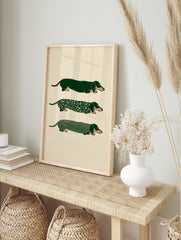 Three illustrative green dachshund dogs, one plain, one floral, one striped, on a light, in an alternate framed mockup